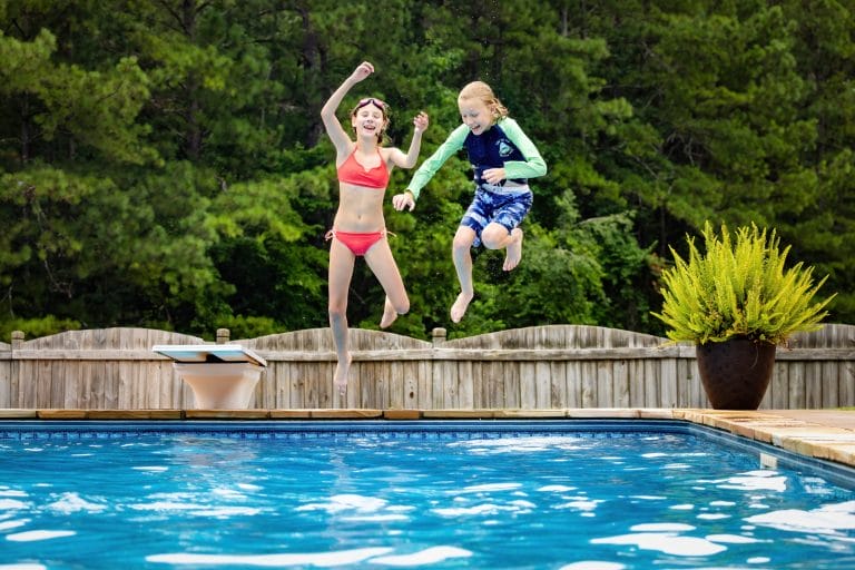 Kids jumping in backyard pool.